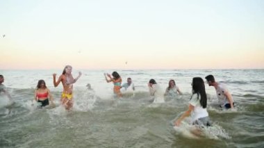 Neşeli insanlar denize su sıçratırken eğlenirler. Erkekler ve kadınlar giyinmiş ve mayo giyip okyanusta oynuyorlar. Arkadaşlar Holi festivalini kutluyor. Tecrit sona erdi, karantina salgını. Yavaş çekim.