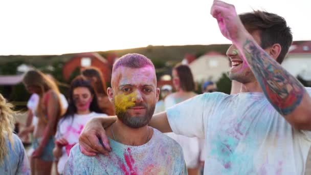 Joyeux gars éclabousse de couleurs sèches sur une autre tête masculine et le frotte dans les cheveux pour le plaisir au festival Holi au ralenti. Deux hommes couverts de poudre colorée jouent des tours. Fin du confinement, pandémie de covidé. — Video