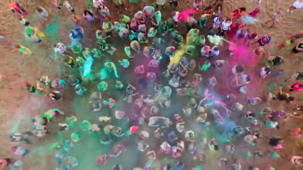 Mariupol, Ucrania - 7 de julio de 2019. Aérea - multitud en el festival holi salpicando polvo de colores. La gente arroja colores secos en el aire de pie sobre la arena para celebrar el festival del amor, la primavera, la unidad. — Vídeos de Stock