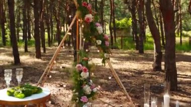 Çam ormanındaki açık hava düğün mekanında konili güzel bir bohem çadır kemeri süslemesi. Sandalyeler, çiçek kompozisyonları güller, halı, ip perisi ışıkları. Yaz kırsal düğünü.
