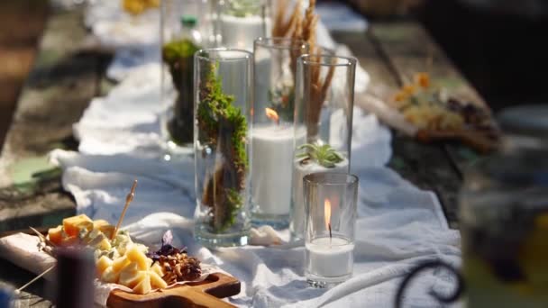 Banquete de boda al aire libre en el bosque. Mesa de comedor decorada en estilo boho con velas, tela blanca, flores, servida con platos, vajilla, platos, comidas, copas y bebidas. catering de vacaciones. — Vídeos de Stock