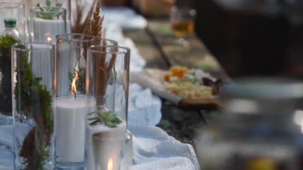 Banquet de mariage en plein air en forêt. Table à manger décorée dans le style boho avec des bougies, tissu blanc, fleurs, servi avec des assiettes, vaisselle, plats, repas, couverts et boissons. Restauration vacances. — Video