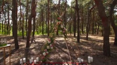 Çam ormanındaki açık hava düğün mekanında konili güzel bir bohem çadır kemeri süslemesi. Sandalyeler, çiçek kompozisyonları güller, halı, ip perisi ışıkları. Yaz kırsal düğünü.