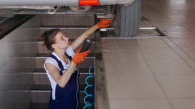 Kadın tamirci uzaktan kumandalı hidrolik tekerlek oyun dedektöründe araba süspansiyonunu inceliyor. Güçlü kadın koşu takımlarında ve direksiyon parçalarında yıpranma olup olmadığını kontrol eder. Tulumlu servis operatörü.
