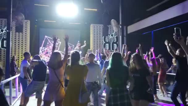 Mariupol, Oekraïne - 25 juli 2021. Mensen dansen en juichen in Barbaris nachtclub. Zanger rapper man of MC treedt op het muziekpodium. Silhouetten van mannen en vrouwen die feesten op de dansvloer. — Stockvideo