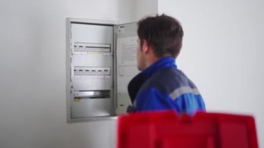 Elektrikçi elektrik sigorta kutusunu söker. Üniformalı usta elektriği tamir etmek için elektrik panelini erteliyor. Tamirci şalterleri ve şalterleri denetleyerek iç sorunları düzeltiyor..