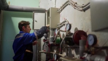 Elektrikçi, sigorta kutusunu inceliyor. Elektriği tamir etmek için elektrik panelini vidalayan üniformalı bir usta. Bölgedeki ısıtma merkezinin teknik odasında kontrol paneli var..