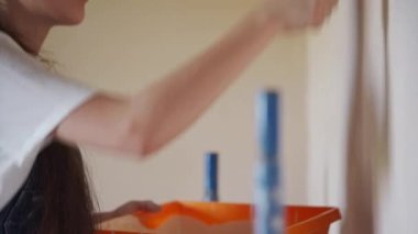 Profesyonel ressam kadın, inşaat alanında duvarı silindir ve tepsiyle boyuyor. Tulumlu ve şapkalı genç bir kadın ev dekorasyonu ve tadilat yapıyor. İşçi odada DIY onarımı yapıyor.