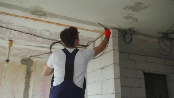 Elektricien legt bedradingskabel, monteert elektriciteitsleidingen in het huis. Bouwer in overalls en handschoenen installeert elektrische draden op de bouwplaats. Man doet appartementenrenovatie. — Stockvideo