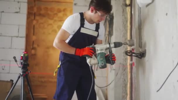 Hombre electricista perforación agujero en la pared para el zócalo utilizando el nivel de láser, taladro de potencia de trabajo, martillo neumático con boquilla cilíndrica. Preparación para instalar cables eléctricos, trabajos de construcción en apartamentos. — Vídeo de stock