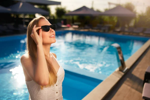 Pretty woman relaxing and sun bathing near swimming pool at luxury spa. Beautiful serene young female model in sunglasses on holiday travel resort enjoying vacation. Sun protection concept. — ストック写真