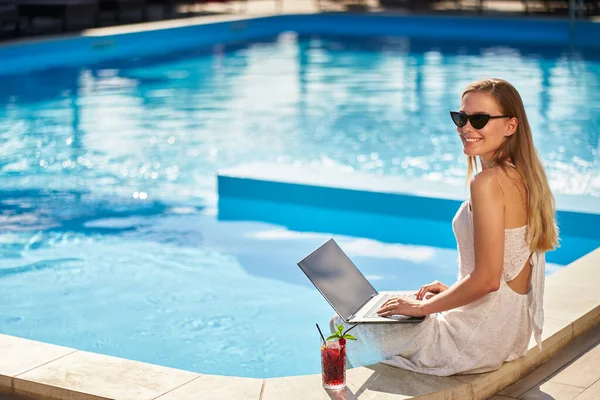 Самозайнята жінка виконує віддалену роботу з ноутбуком, сидячи біля басейну в тропічному спа-центрі з коктейльним напоєм. Фрілансер бізнес-леді телекомунікації з командою на проекті від розкішного курорту . — стокове фото