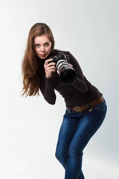 一个漂亮的摄影师女孩，带着专业的飞镖相机，在工作室的白色背景上摆姿势。照片学习、学习、培训概念 — 图库照片