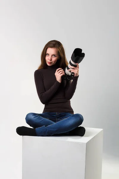 一个漂亮的摄影师女孩，带着专业的飞镖相机，在工作室的白色背景上摆姿势。照片学习、学习、培训概念 — 图库照片
