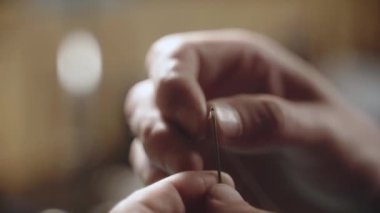 Erkek eli iğneye iplik geçirir. Dikiş ve terzilikte operasyon detayları. Erkek parmakları bulanık arkaplan ile iğne ve iplik kullanır.