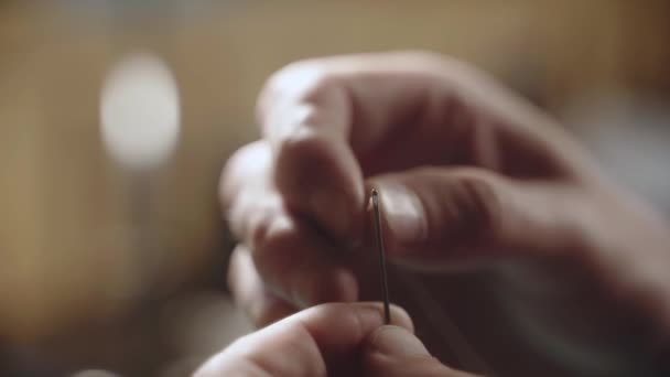 Close-up male hands thread a needle. Operational details at sewing and tailoring. Mans fingers use needle and thread with a blurred background. — Video