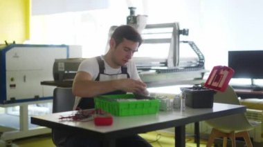 Elektrikçi, elektrik paneli sigorta kutusunu atölyede monte ediyor. İşçi masadaki dağıtım panosuna enerji sayacı, şalterler ve devre kesiciler kurar.