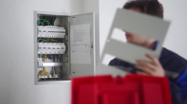 Elektrikçi sigorta kutusunu monte ediyor. Üniformalı usta elektrik sorunlarını çözdükten sonra elektrik paneli takıyor. Tamirci şalterleri ve şalterleri kontrol ederek ev içi sorunları düzeltiyor..