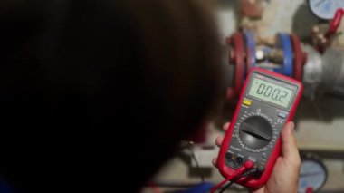 Elektrikçi, bölgesel ısıtma istasyonunda çoklu sayaçlı sigorta kutusundaki voltajı kontrol ediyor. Üniformalı uzman, kontrol panelini elektiriği tamir etmek için test eden sondalarla inceliyor. Teknik odadaki adam..