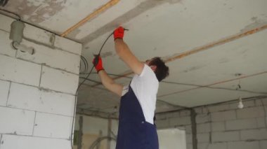 Elektrikçi kabloları döşeyip, eve elektrik kabloları yerleştiriyor. Tulum ve eldiven giyen inşaatçı inşaat alanına elektrik kabloları yerleştiriyor. Daire tadilatı yapan adam..