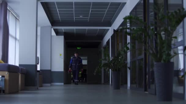 Électricien répare lumière dans le bureau. Les finitions principales fonctionnent avec l'électricité. Serrurier marchant le long du hall du centre d'affaires avec boîte à outils. L'homme va postuler pour le poste d'ingénieur. Mécanicien masculin en uniforme. — Video