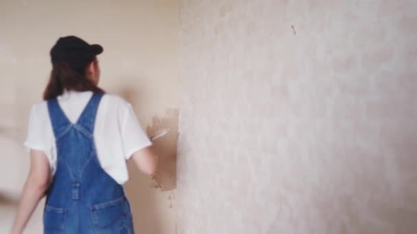 专业的灰泥匠女性会在墙壁上打孔，涂上石膏，并在工作服和球帽的水沫上撒布。年轻的女石膏墙壁，在建筑工地做装修工作。职业：. — 图库视频影像