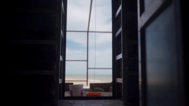 Woman in jumpsuit with a spatula and bucket of plaster or putty enters the doorway of construction site. Plasterer starts working day. Silhouette of repairwoman gets into a building. — Vídeo de Stock