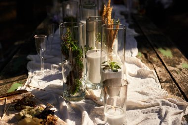 Düğün partisi dışarıda ormanda ziyafet veriyor. Mum, beyaz kumaş, çiçek, tabak, sofra takımı, yemek takımı, yemek takımı, kadeh ve içeceklerle süslenmiş yemek masası. Tatil yemekleri..