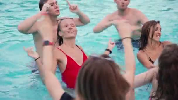 Amigos tienen fiesta en la piscina nocturna en una piscina villa privada. Jóvenes felices en traje de baño salpicando agua, bailando con flotadores y colchón inflable en resort de lujo. — Vídeo de stock