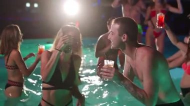 Arkadaşların özel bir yüzme havuzunda gece havuzu partisi var. Mayo giymiş neşeli genç insanlar su sıçratıyor, dans ediyor ve lüks otellerde parti yapıyorlar. Mutlu erkekler ve kadınlar birlikte takılıyor. Yavaş çekim.