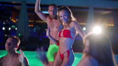 Arkadaşların özel bir yüzme havuzunda gece havuzu partisi var. Mayo giymiş neşeli genç insanlar su sıçratıyor, dans ediyor ve lüks otellerde parti yapıyorlar. Mutlu erkekler ve kadınlar birlikte takılıyor. Yavaş çekim.