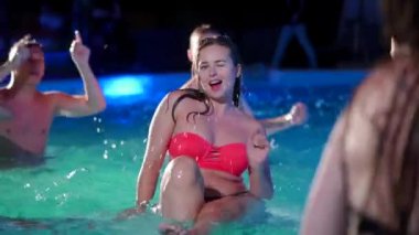 Bikinili çekici bir kadın gece havuz partisinde arkadaşlarıyla flört ediyor. Lüks bir özel villada havuzda eğlenen çekici bir kadın. Oyuncak kadın yavaş çekimde göz kırpar.