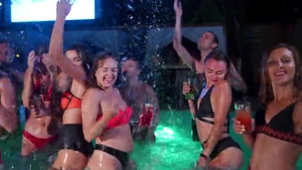 Hot women toast, clink glasses with cocktails at night pool party. Female friends clubbing and partying. Cheerful girls in swimwear drink beverages, dance in luxury resort villa. Slow motion. — Video Stock
