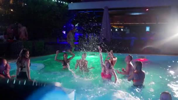 Друзья устраивают вечеринку у бассейна в частном бассейне виллы. Веселые молодые люди в купальниках брызгают водой, танцуют и веселятся на роскошном курорте. Счастливые мужчины и женщины тусуются. Медленное движение. — стоковое видео