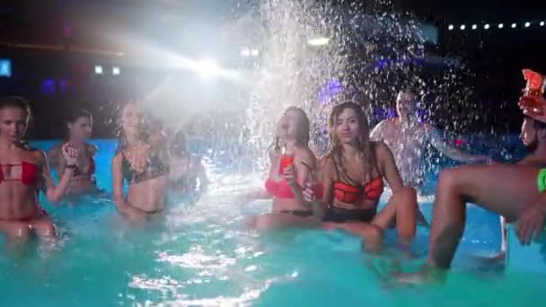 Friends splashing water at night pool party swimming pool. Cheerful young people in swimwear partying, dancing and partying in luxury resort villa. Happy men and women hanging out. Slow motion. — Video Stock