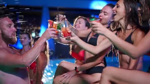 Vrienden toasten, klinkende glazen met cocktails op het nachtzwembadfeest. Vrolijke mensen in badmode drinken drankjes, dansen, clubben en feesten in luxe resort villa. Langzame beweging. — Stockvideo