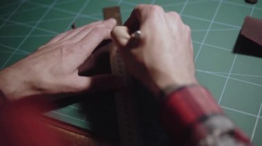 Yakın plan eller bıçakla deri desenleri oyar ve fazlalık kısımları çıkartır. Tanner, terzi tezgahın arkasında çalışıyor ve deri eşyalar yapıyor. El yapımı..