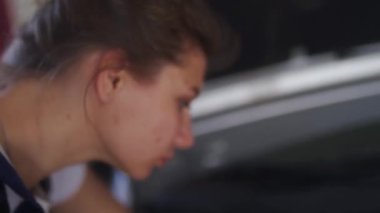 Kadın tamirci kaputun altındaki araba parçalarını inceliyor. Tulumlu bir kadın araba tamir servisindeki motor ve parçaları kontrol ediyor. Modern atölyede araç tamiri hatası.