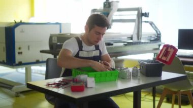 Elektrikçi, elektrik paneli sigorta kutusunu atölyede monte ediyor. İşçi masadaki dağıtım panosuna enerji sayacı, şalterler ve devre kesiciler kurar.