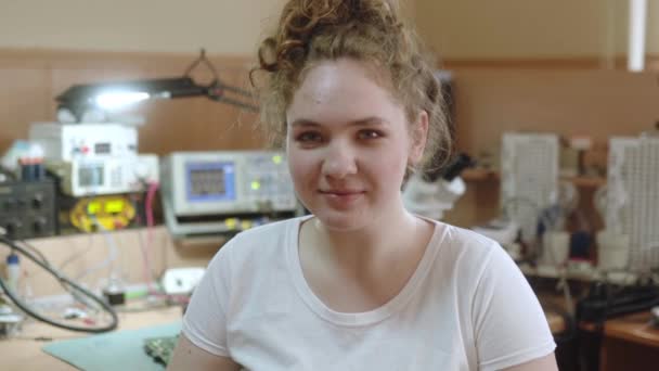 Heureuse travailleuse sourit à une caméra à l'atelier de réparation électronique. Femme fixe les appareils ménagers, les ordinateurs et le matériel électrique dans son atelier. — Video