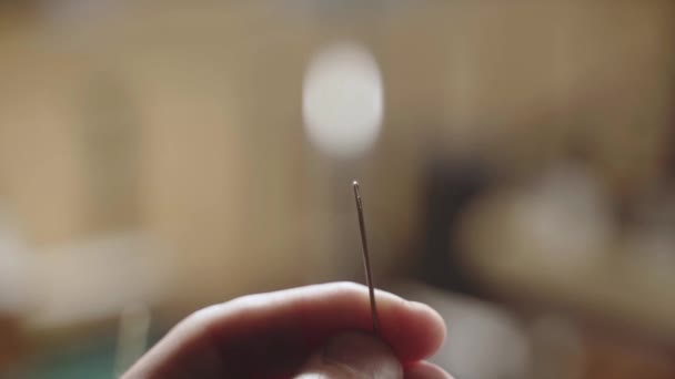 Close-up male hands thread a needle. Operational details at sewing and tailoring. Mans fingers use needle and thread with a blurred background. — Video