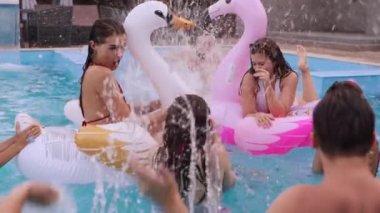 Arkadaşlar havuzda su sıçratan havuz partisi yaparlar. Mayo dansındaki neşeli gençler, şamandıralarla parti, şişme flamingo, lüks oteldeki kuğu. Bikinili ıslak kızlar ağır çekimde.