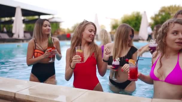 Gadis berbikini mengadakan pesta kolam renang dengan koktail di kolam renang. Wanita santai gelas dentingan dengan minuman di resor mewah. Teman-teman wanita dalam tarian baju renang merah, klub di dalam air. Gerakan lambat. — Stok Video