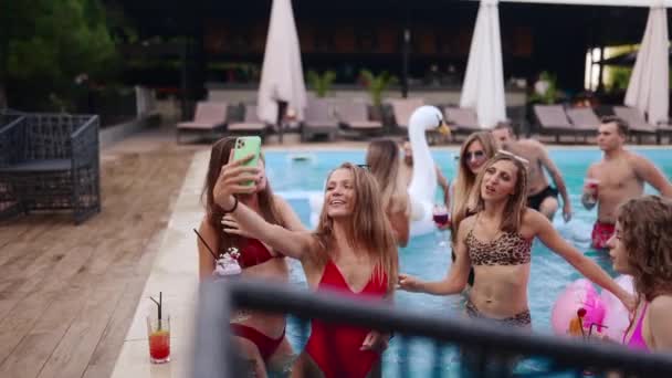 Travel blogger woman in bikini taking selfie photo with friends in swimming pool party. Lifestyle vlogger films vlog with hot girls from luxury resort. Female live streaming on social media. — Stockvideo