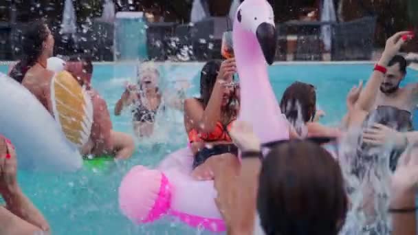 Friends have night pool party in a private villa swimming pool. Happy young people in swimwear splashing water, dancing with floaties and inflatable mattress in luxury resort. Slow motion. — Stockvideo