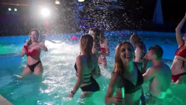 Vrienden hebben nachtzwembadfeest in een privé villa zwembad. Vrolijke jongeren in zwemkleding spetterend water, dansen en feesten in luxe resort. Gelukkige mannen en vrouwen die rondhangen. Langzame beweging. — Stockvideo