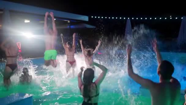 Друзья танцуют у бассейна в частном бассейне виллы. Веселые молодые люди в купальниках прыгают и ныряют с брызгами воды в роскошном курорте. Мужчины и женщины тусуются в замедленной съемке. — стоковое видео