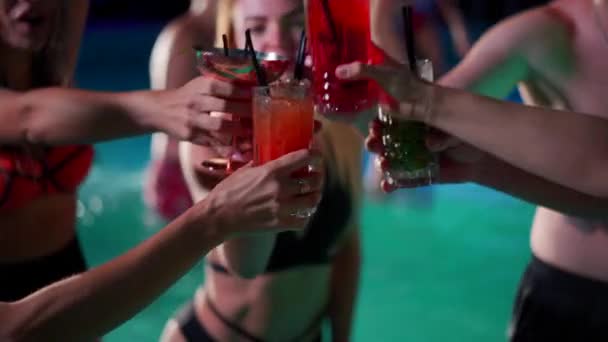 Vrienden toasten, klinkende glazen met cocktails op het nachtzwembadfeest. Vrolijke mensen in badmode drinken drankjes, dansen, clubben en feesten in luxe resort villa. Langzame beweging. — Stockvideo