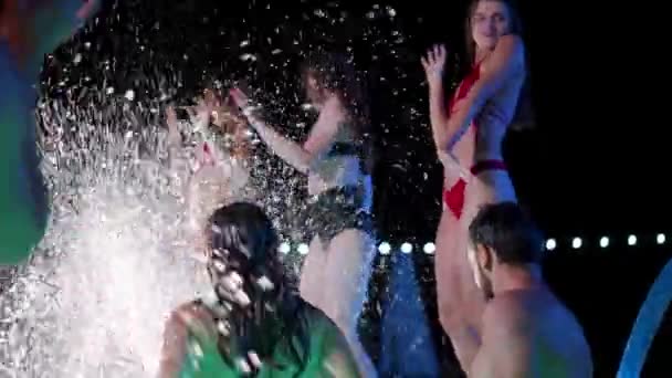 Vrienden spetteren water in het nachtbad feestbad zwembad. Vrolijke jongeren in zwemkleding feesten, dansen en feesten in luxe resort villa. Gelukkige mannen en vrouwen die rondhangen. Langzame beweging. — Stockvideo