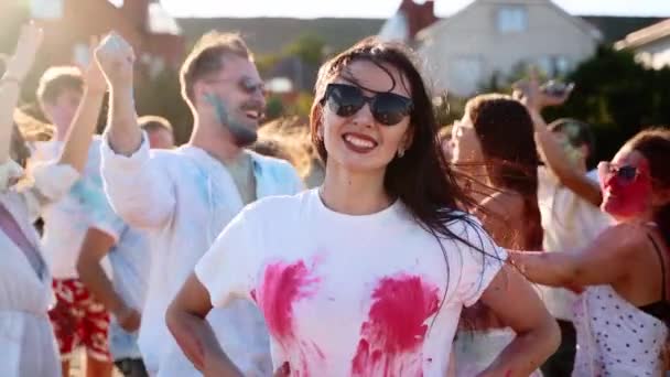 Mooie vrouw spettert gekleurd poeder op haar witte T-shirt op borsten gebied. Meisje met zonnebril heeft plezier op Holi festival. Mensen vieren hindoeïstische feestdagen. Einde van de afsluiting, hevige pandemie, beperkingen. — Stockvideo